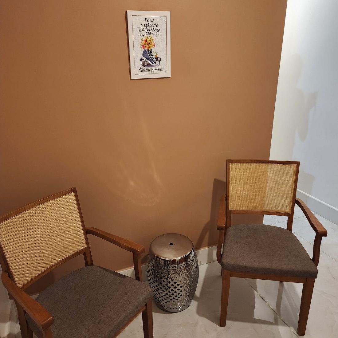 Sala de espera do consultório: parede terracota, cadeiras de madeira e palhinha e um quadro na parede